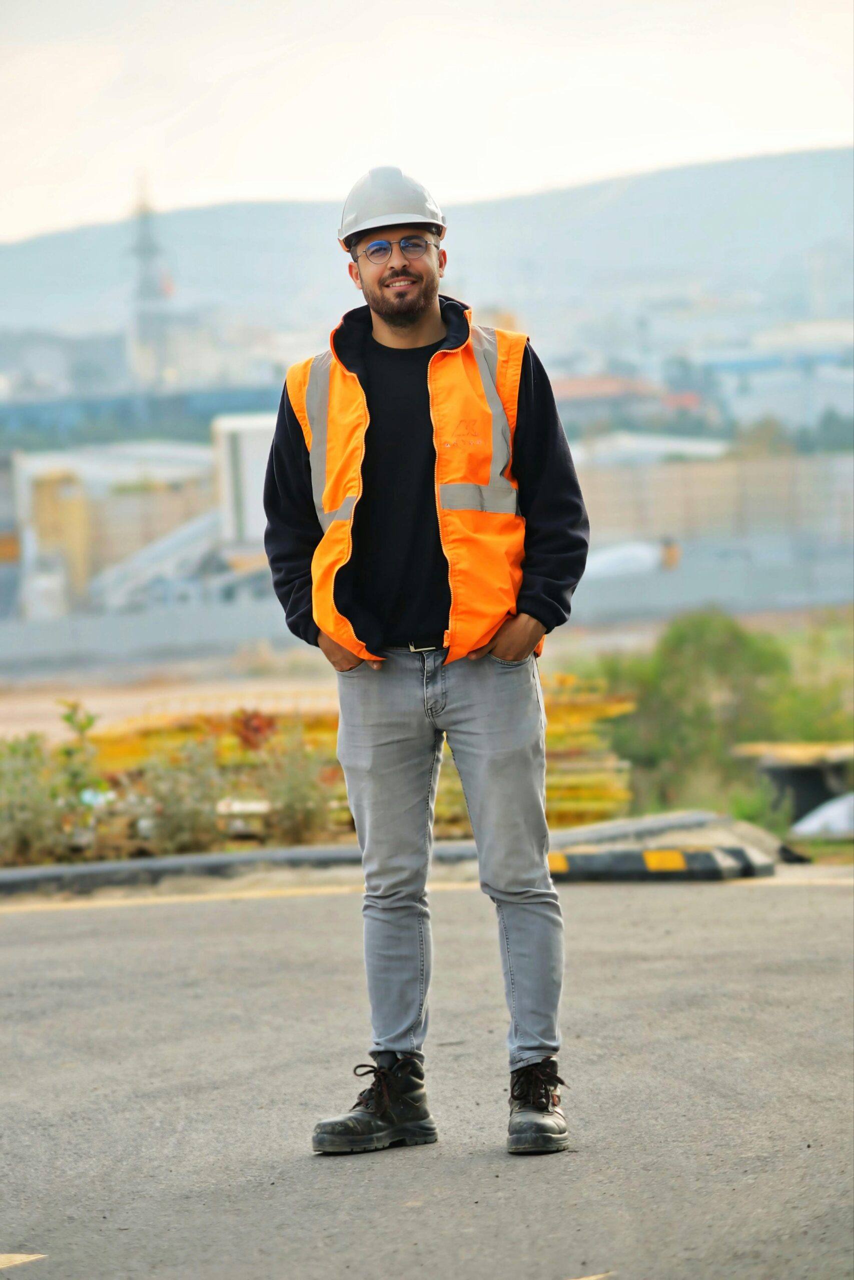A construction worker stands confidently outdoors wearing safety gear and helmet.
